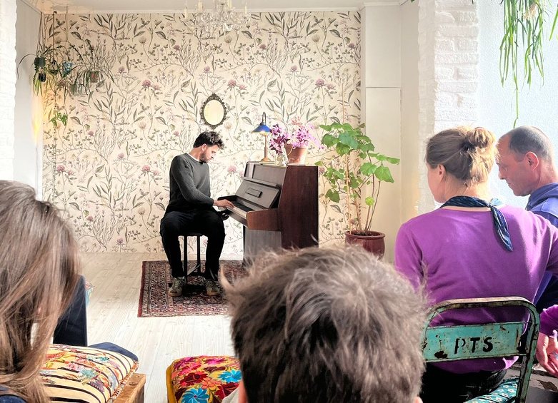 Iemand speelt piano voor een groepje bezoekers in een woonkamer